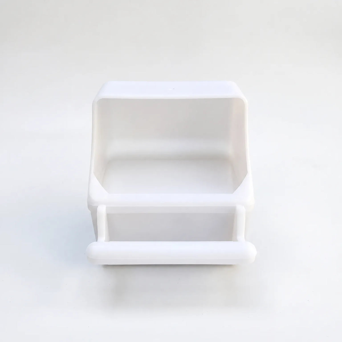 White plastic seed feeder seen from the front on a plain background, showing the open hopper and the rounded perch below. 1