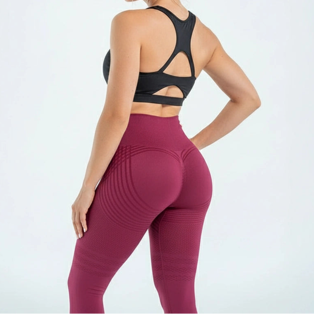Back view of a model in burgundy leggings with a scrunched seam and curved stripes, worn with a black racerback sports bra. 6