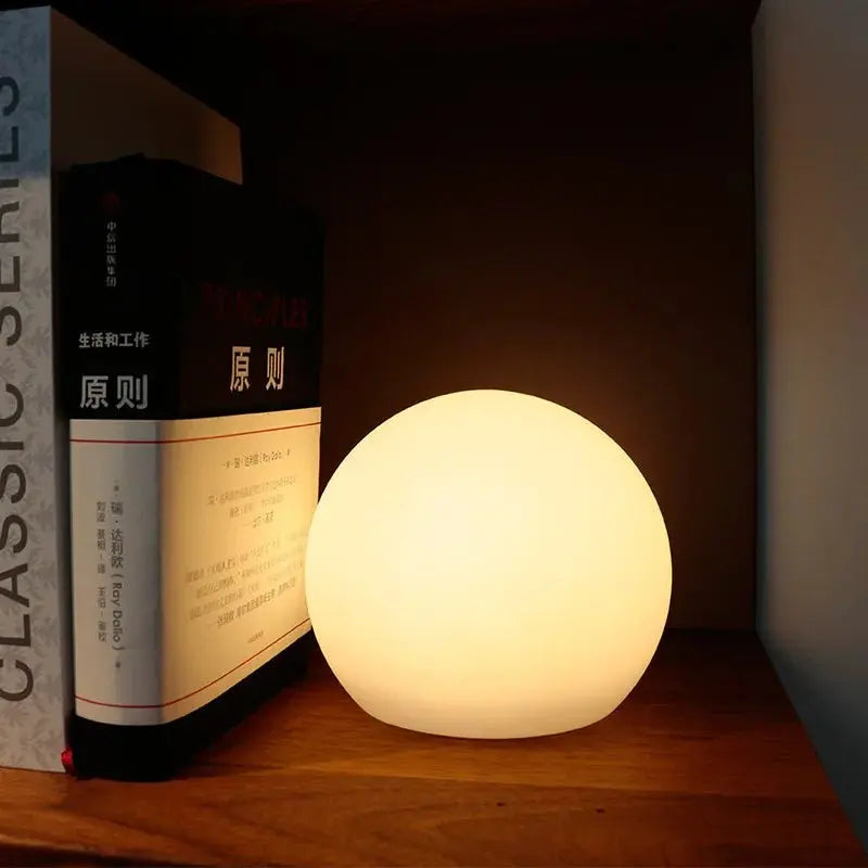 Warm glowing orb lamp tucked beside upright books on a dark wooden shelf, lighting the nook at night. 4