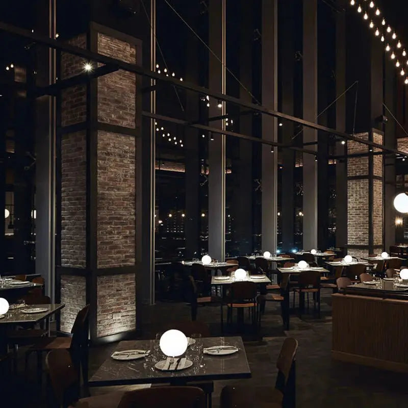 Dimly lit restaurant with brick pillars, where small glowing orb lamps sit on many of the dining tables. 8