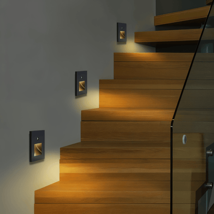 Three dark square wall lights lighting a wooden staircase with a glass balustrade in warm tones 3