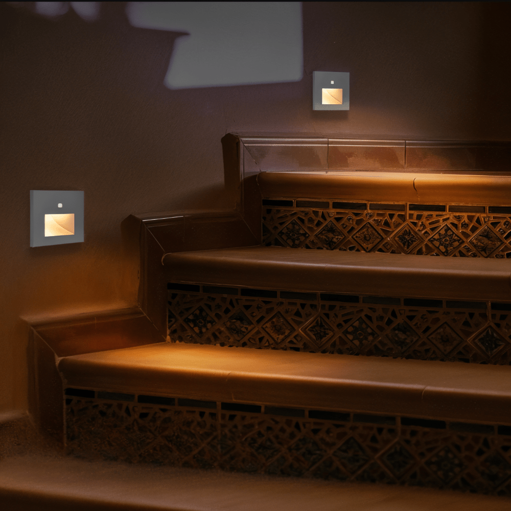 Two light grey square wall lights casting warm glow over ornate tiled stair risers 4
