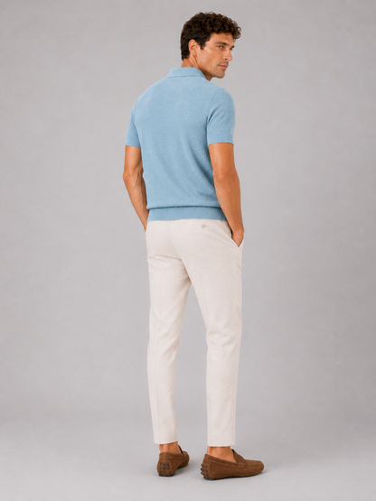 Back view of model wearing light blue knit polo with cream trousers and brown driving loafers 4