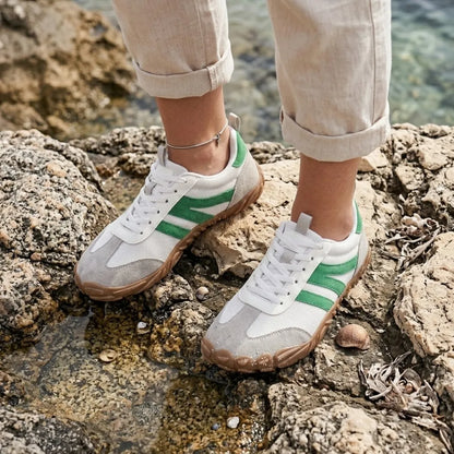 Woman wearing the white and green shoes while standing on coastal rocks beside shallow water, with rolled linen trousers. 29