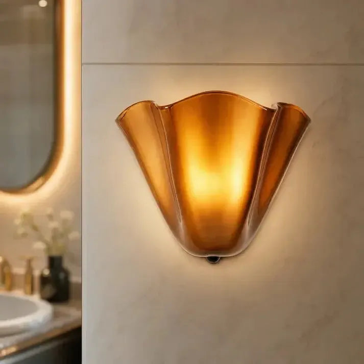 Lit amber glass sconce glowing warmly on a marble-effect bathroom wall, with a mirror and basin softly blurred beside it. 10