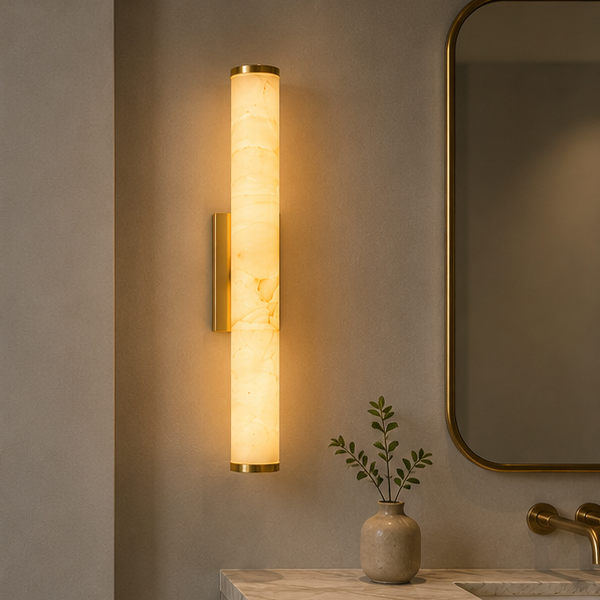 Single lit marble wall light with brass-tone caps and bracket above a bathroom vanity, beside a gold-framed mirror and a small plant. 2