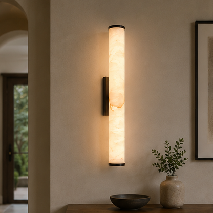 Dark-capped marble wall light in a hallway above a wooden console with a bowl and a vase of greenery, framed art alongside. 11