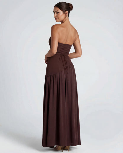 Back view of brown strapless maxi showing corset lacing at the waist and gathered skirt, model glancing over shoulder 2