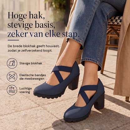 Navy block heels with crossed elastic straps worn by a seated woman in jeans and a trench coat on a paved street. 1