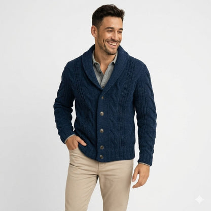 Smiling man in the navy cable-knit shawl-collar cardigan, three-quarter view against a plain white background, one hand in his beige trouser pocket. 1