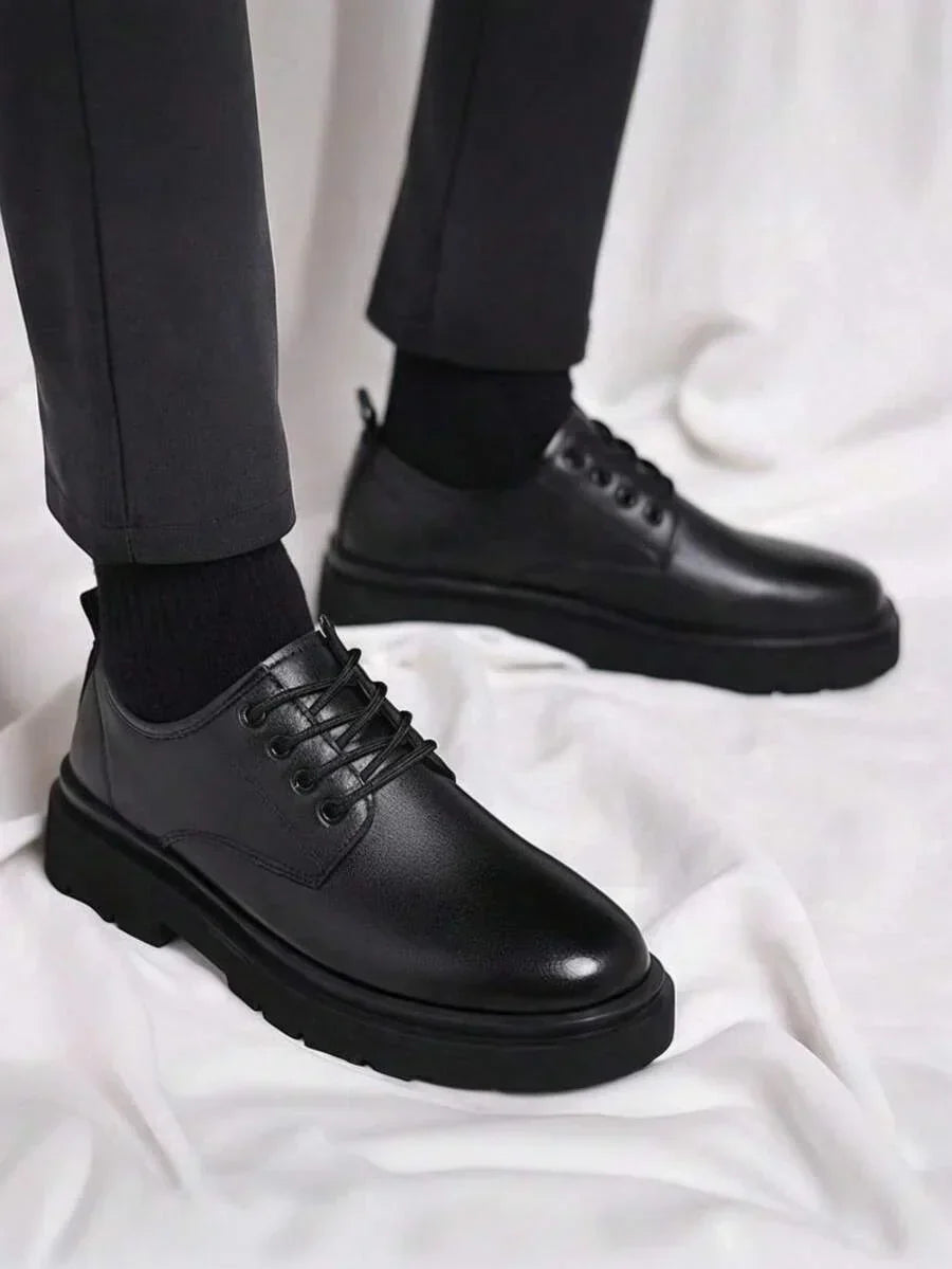 Pair of lace-up derby shoes worn with dark trousers and black socks on white fabric 1