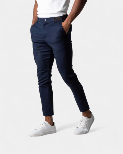 Model wearing navy slim tapered trousers with white trainers and a white top, hands in pockets 2