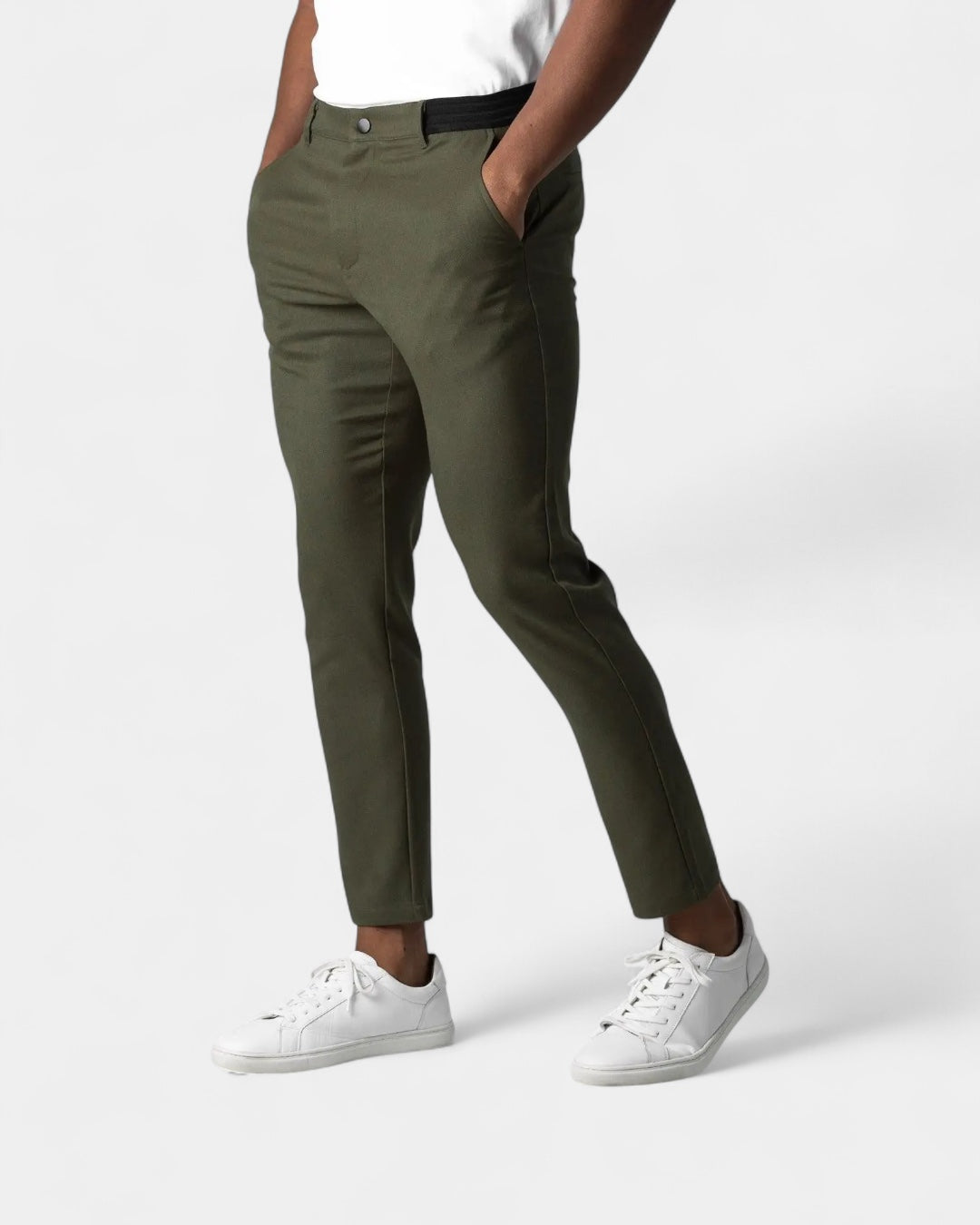 Model wearing olive green slim tapered trousers with white trainers, hands in pockets, shown from the front 4