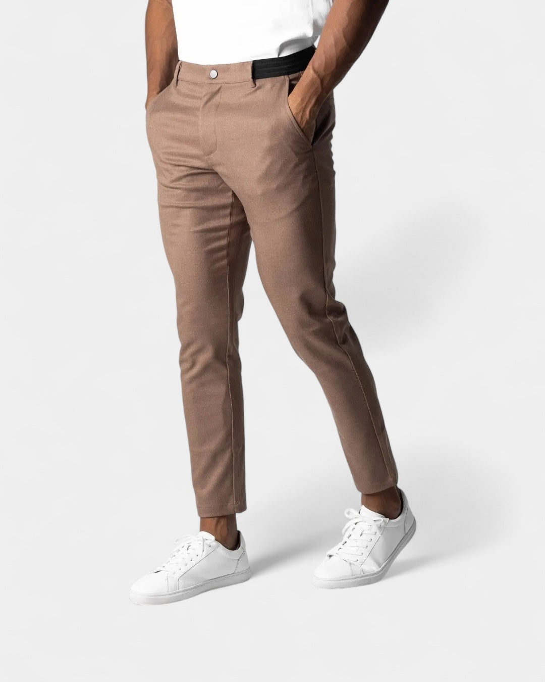 Model wearing light brown slim tapered trousers with white trainers and a white top, hands in pockets 5