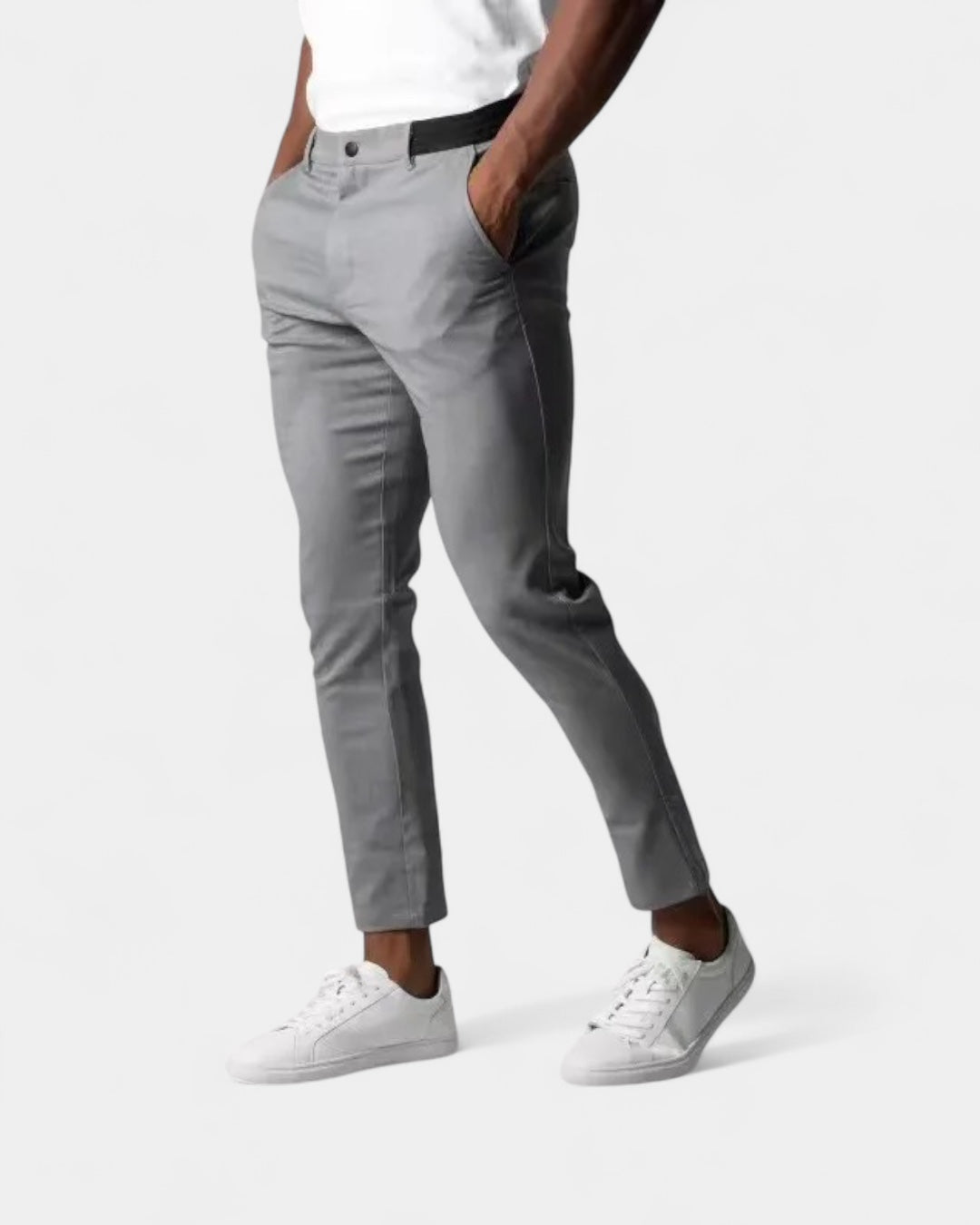 Model wearing light grey slim tapered trousers with white trainers, one hand in pocket, seen from the front 1