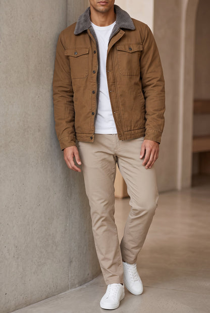Model leaning against a concrete wall wearing the tan jacket over a white tee and beige trousers 2