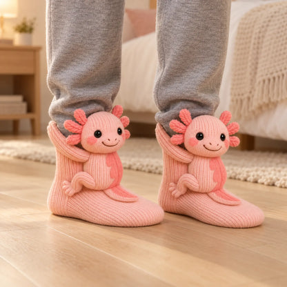 Pair of pink knitted socks with smiling axolotl figures, worn with grey joggers in a bedroom 1