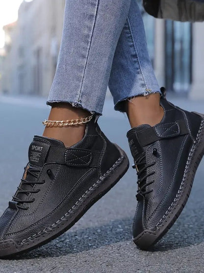 Close-up of a model's feet in black stitched trainers with laces, worn with frayed jeans and a gold anklet 5