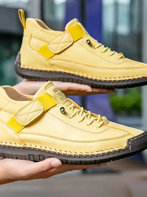 Two hands hold a pair of pale yellow shoes with hook-and-loop straps, laces and dark stitched soles 15