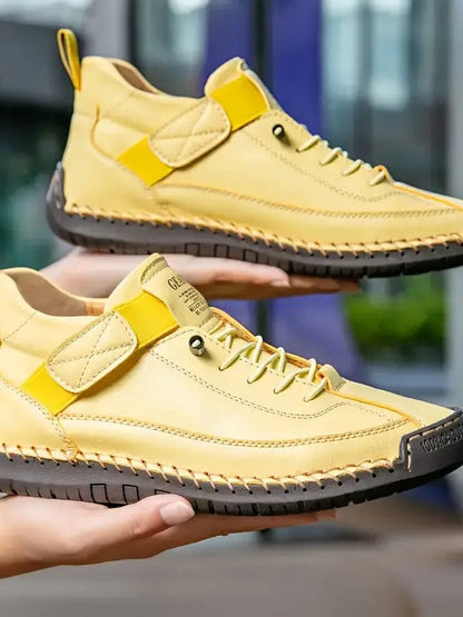 Two hands hold a pair of pale yellow shoes with hook-and-loop straps, laces and dark stitched soles 15