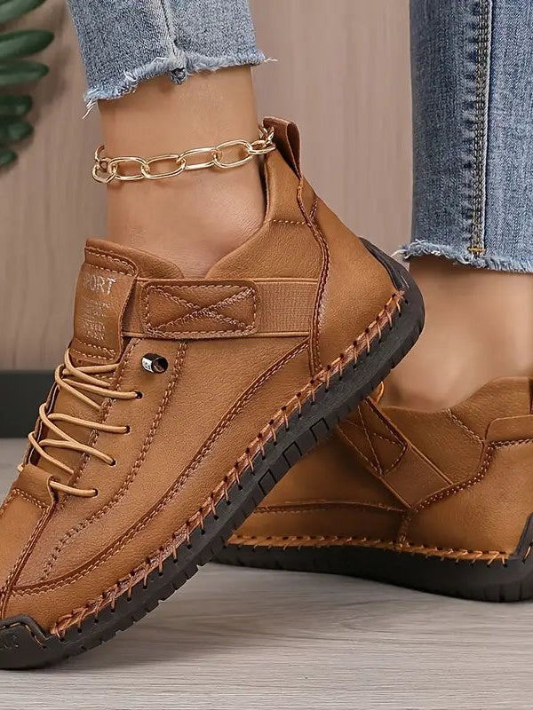 Worn close-up of tan stitched shoes with laces, a hook-and-loop strap and a dark sole, with a gold ankle chain 7
