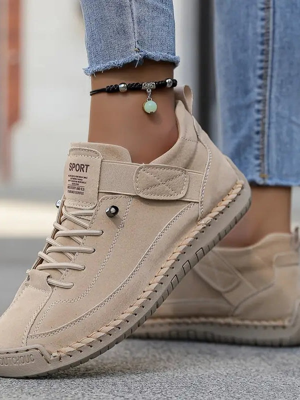 Close-up of a beige suede-look trainer with elastic laces and stitched edging, worn with rolled jeans and an anklet 14