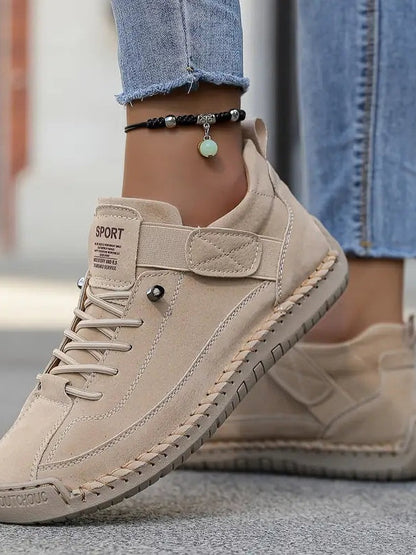 Close-up of a beige suede-look trainer with elastic laces and stitched edging, worn with rolled jeans and an anklet 14