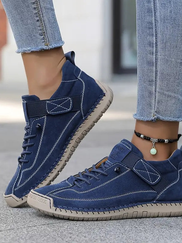 Close-up of navy suede-look trainers with white stitching, elastic strap and beige sole, worn with cropped jeans and an 3