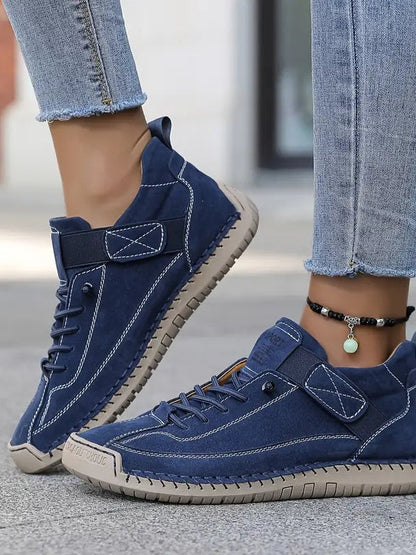 Close-up of navy suede-look trainers with white stitching, elastic strap and beige sole, worn with cropped jeans and an 3