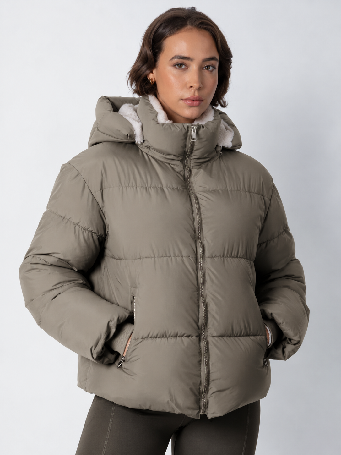 Model wears the taupe-grey puffer jacket zipped up with the hood on, hands in the zipped pockets 18