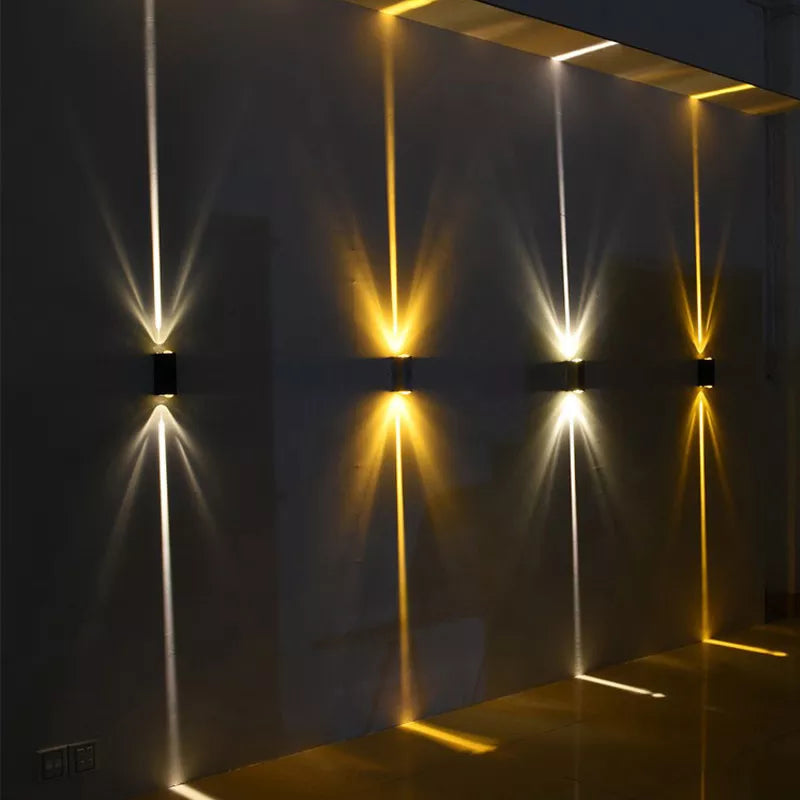Four small black wall lights casting narrow beams of white and warm yellow light up and down a dark wall 1