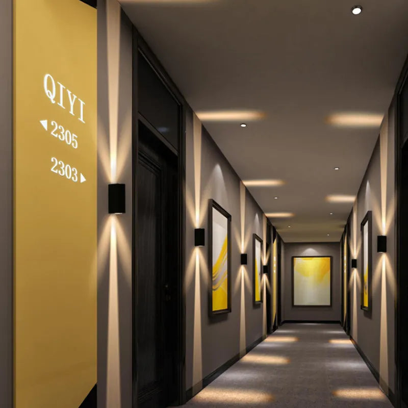 Black wall lights spaced along a hotel corridor, casting narrow vertical beams of warm light on grey walls 2