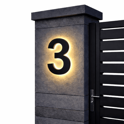 Black number 3 with a warm backlit glow on a dark stone gatepost next to a black slatted gate. 9