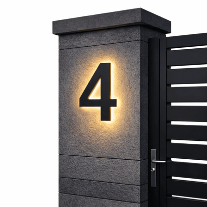Black number 4 with a warm backlit glow on a dark stone gatepost next to a black slatted gate. 10