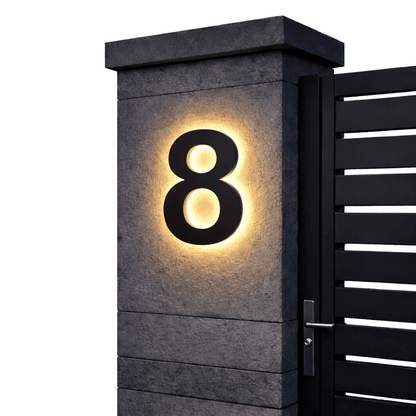 Black number 8 with a warm backlit glow on a dark stone gatepost next to a black slatted gate. 11