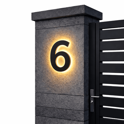 Black number 6 with a warm backlit glow on a dark stone gatepost next to a black slatted gate. 12