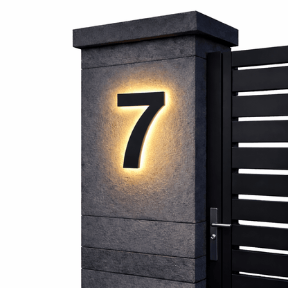 Black number 7 with a warm backlit glow on a dark stone gatepost next to a black slatted gate. 13