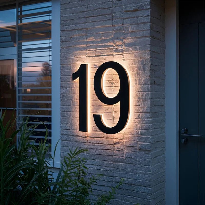 Black number 19 with warm backlighting mounted on a white-painted brick wall next to a dark front door. 4