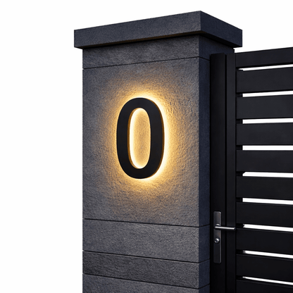 Black number 0 with a warm backlit glow on a dark stone gatepost next to a black slatted gate. 6