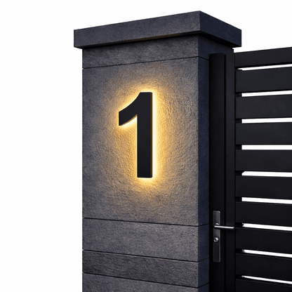 Black number 1 glowing with warm backlight on a dark textured stone gatepost beside a slatted black gate. 1