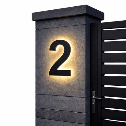 Black number 2 with a warm backlit glow on a dark stone gatepost next to a black slatted gate. 7