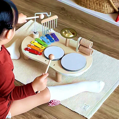 Child in a red top sits on a rug, striking a drum with a mallet 2