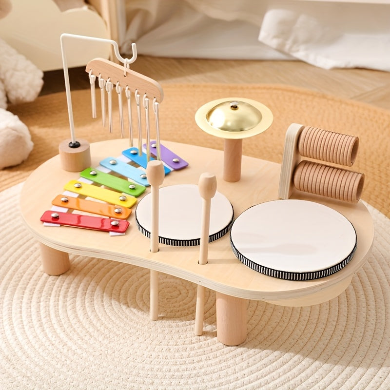 Wooden music table set up on a woven rug, with rainbow xylophone, two drums, cymbal, chimes and wooden tubes. 1