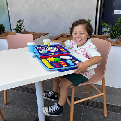 Laughing boy at an outdoor table with the blue book open, showing clock, gears and zip pages 7