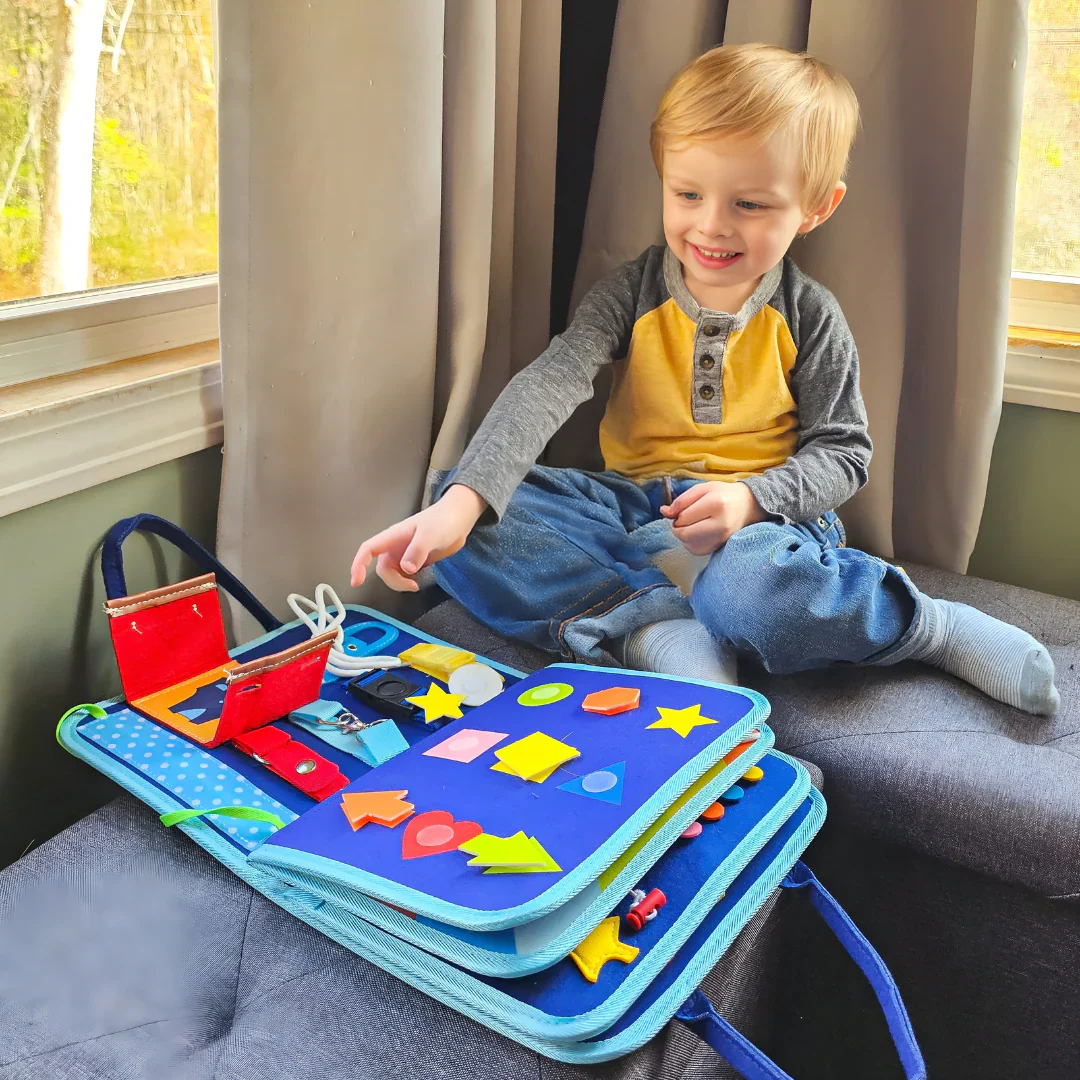Smiling blond toddler sits on a sofa by a window, playing with the blue felt book 3
