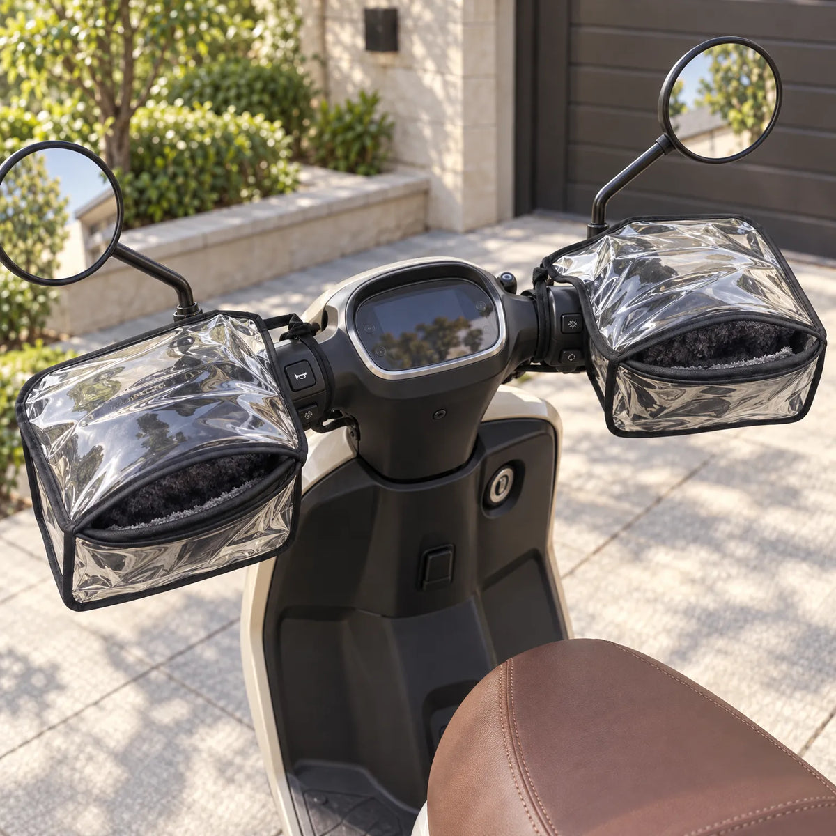 Pair of clear handlebar muffs with fleece lining fitted to a cream scooter parked on a sunlit paved drive. 1