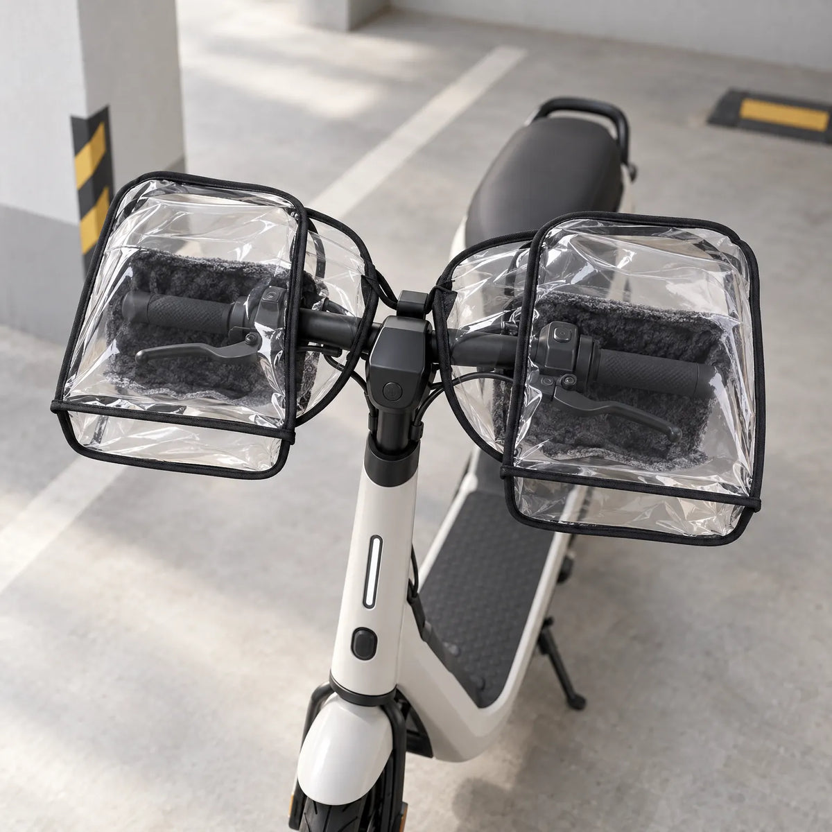 Clear muffs with soft grey fleece lining fitted over the grips and brake levers of a white scooter in a car park. 3