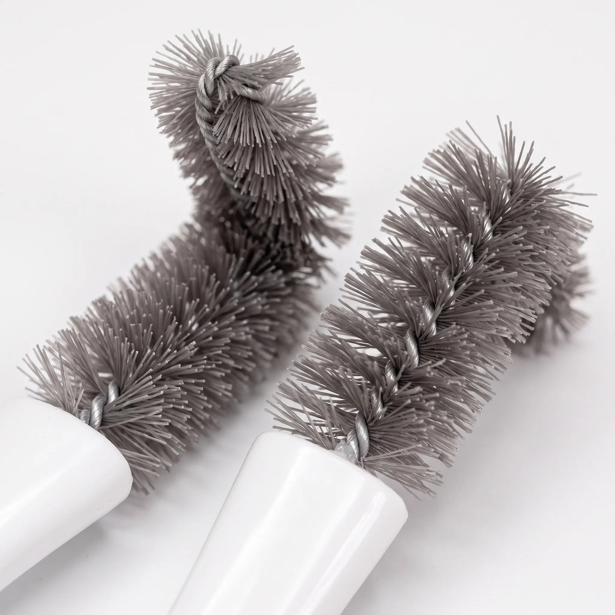 Close-up of two grey twisted-wire bristle heads, one bent at an angle, joined to white handles. 3
