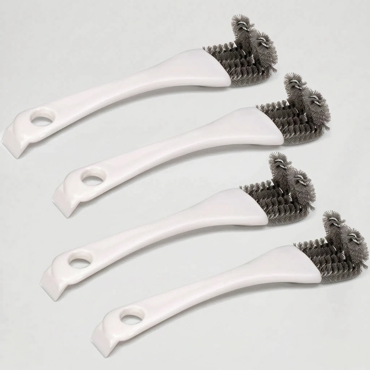 Four white brushes laid at a diagonal on a pale surface, showing the grey bristle heads, hanging holes and scraper ends. 4