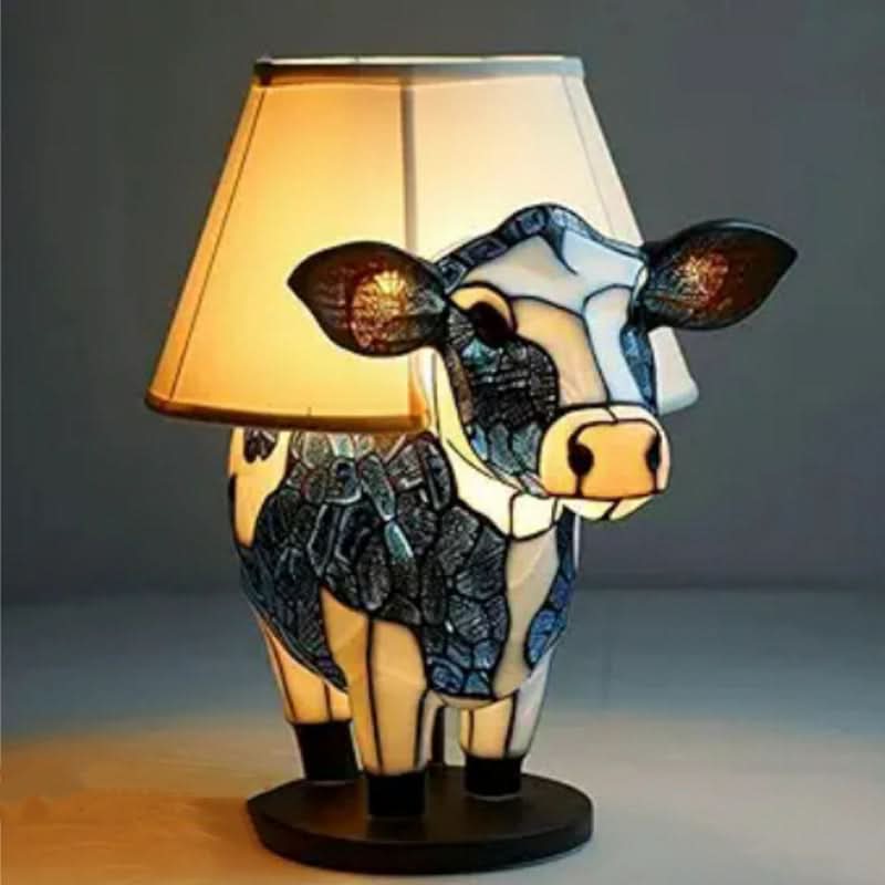 Cow lamp with blue and white glass body standing on a round dark base, fitted with a cream fabric lampshade. 12
